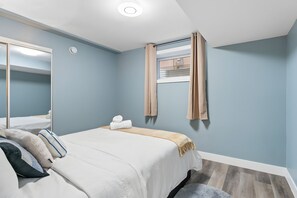 Une chambre à coucher avec un lit, un miroir, une fenêtre avec des rideaux et un luminaire au plafond.