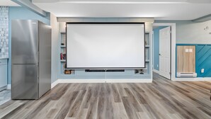 Moderni keittiö, jossa on sisäänrakennettu jääkaappi, suuri litteänäyttöinen televisio ja puulattia.