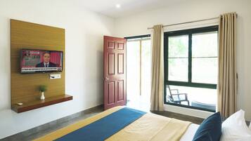 A hotel room with a bed, a TV mounted on the wall, a door, and a window with curtains.