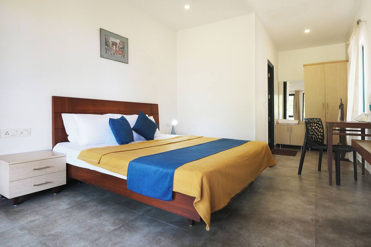A neatly arranged hotel room with a bed, bedside table, and a desk with a chair.