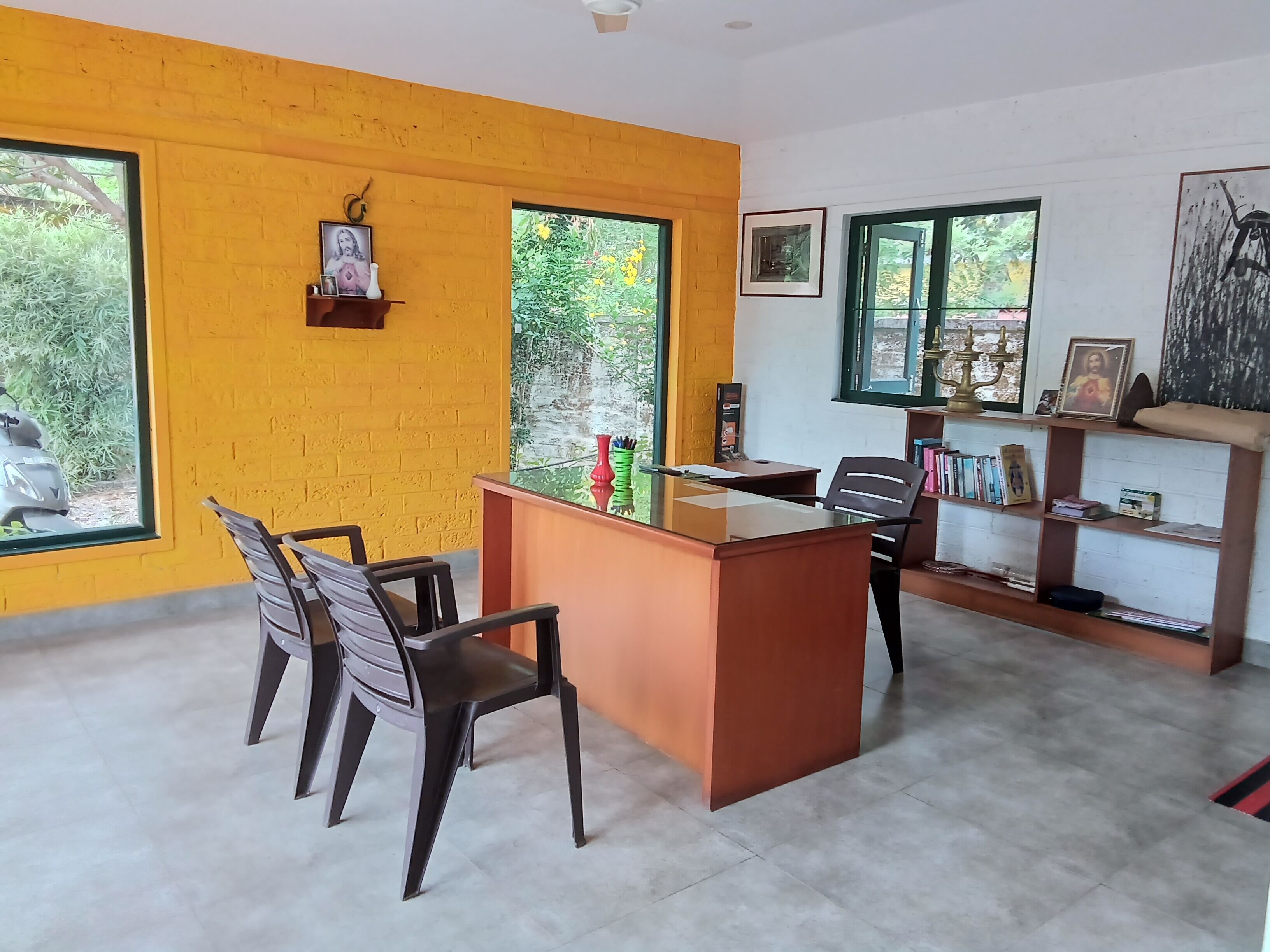 A room with a desk, two chairs, a bookshelf, and large windows.