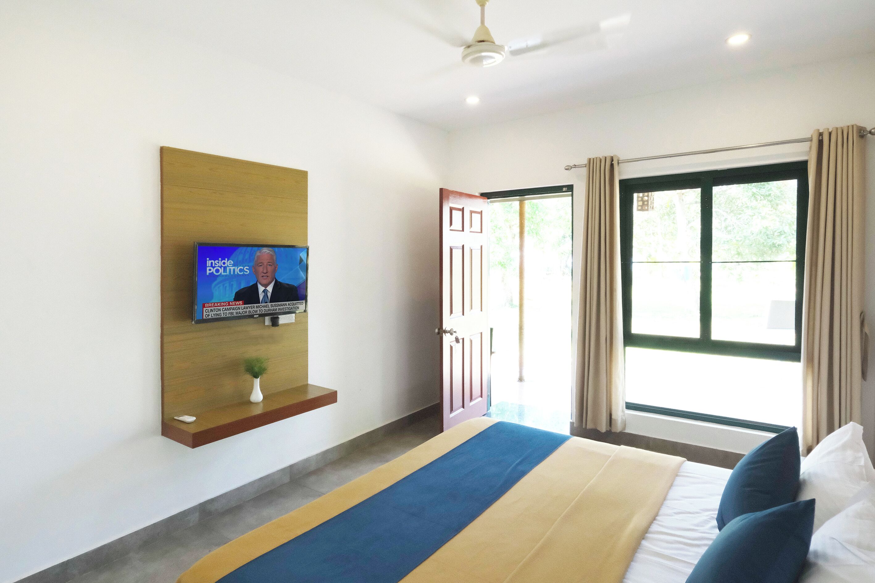 A hotel room with a bed, a television mounted on the wall, a door leading outside, and a window with curtains.