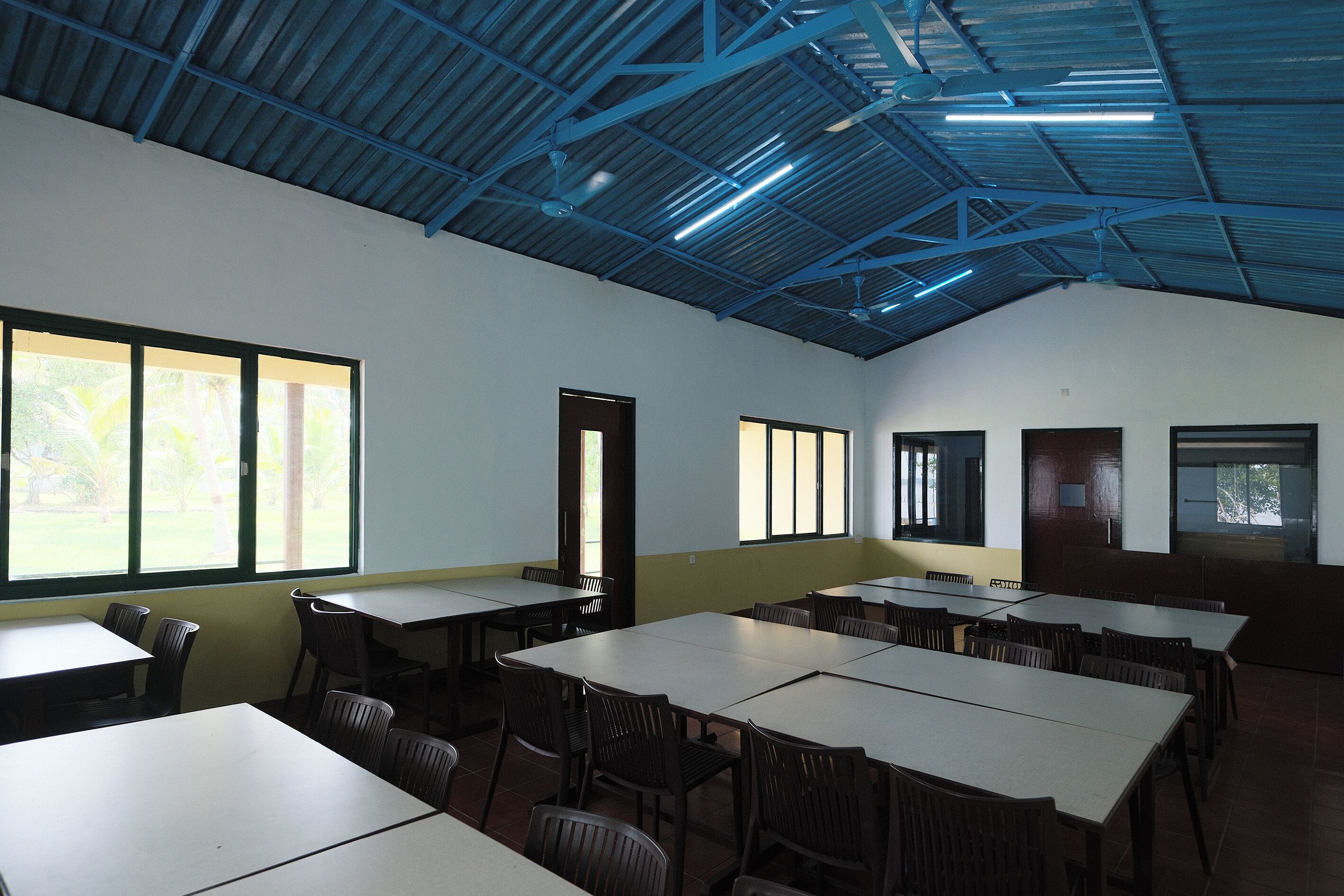 Une salle de conférence équipée de tables et de chaises, dotée de grandes fenêtres et d’un plafond haut avec des poutres apparentes.