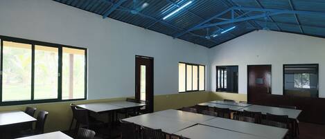 Une salle de conférence équipée de tables et de chaises, dotée de grandes fenêtres et d’un plafond haut avec des poutres apparentes.