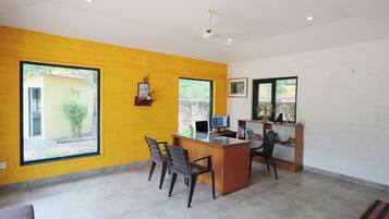 Quarto com escrivaninha, duas cadeiras, computador e janela com vista para área verde.