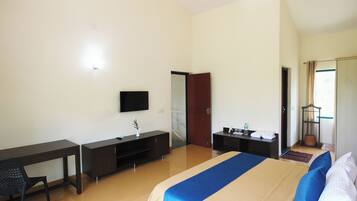 A hotel room with a bed, desk, chair, TV, wardrobe, and a small table with a lamp.