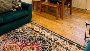 Una sala de estar acogedora con un sofá color turquesa, una mesa de comedor de madera y una alfombra colorida.
