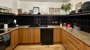 Una cocina con armarios de madera, lavavajillas negro, encimera de granito y azulejos tipo metro negros.