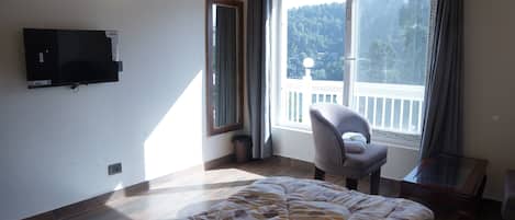A bedroom with a bed, a chair, a TV, and a window with a view of trees.