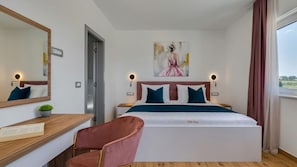 A hotel room with a bed, a desk, a chair, a mirror, and a painting on the wall.