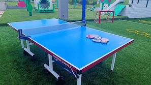 A ping pong table with a net, surrounded by artificial grass, in an outdoor recreational area.