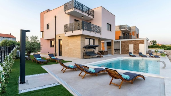 A modern two-story house with a swimming pool, outdoor seating, and a well-maintained garden.