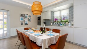 A dining area with a table set for four, a hanging light fixture, and a kitchen in the background.