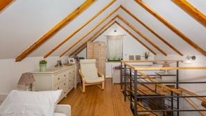 Una camera da letto mansardata accogliente con travi a vista in legno, un letto, una sedia, una scrivania e una scala.