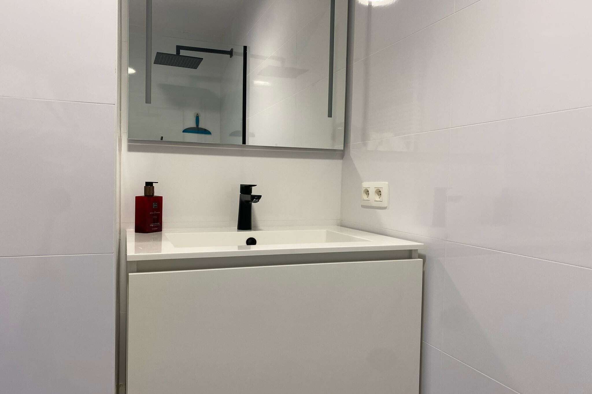 Ein modernes Badezimmer mit einem weißen Waschbecken, einem schwarzen Wasserhahn und einem roten Seifenspender.