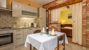 Une cuisine compacte dotée d’appareils électroménagers modernes, un coin repas avec une table blanche dressée pour deux personnes et un mur de briques chaleureux.