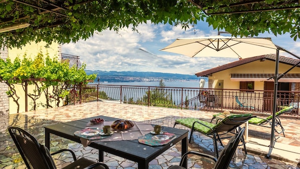 A patio with a table set for two, a view of the sea, and a building with a balcony.