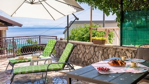 Una terraza con mobiliario exterior, una mesa con comida y vista al mar.