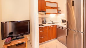 A compact kitchen with a flat-screen TV, wooden cabinets, a stainless steel refrigerator, and a coffee maker.