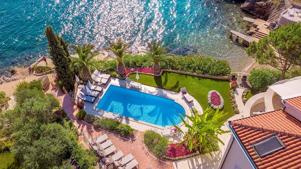 A swimming pool with sun loungers and a garden area, surrounded by a stone wall and overlooking a body of water.