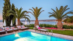 Une piscine bordée de chaises longues et de parasols, des palmiers et une vue sur la mer.