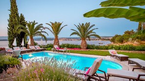 Ein Pool mit Liegestühlen, umgeben von Grün und Blick aufs Meer.