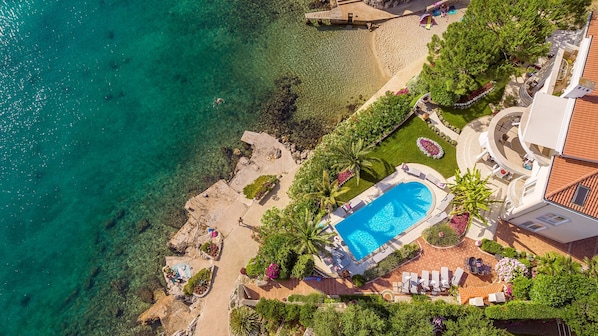 An aerial view of a resort with a swimming pool, beach, and lush landscaping.