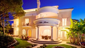 A large, elegant house with a central circular patio, a balcony, and a well-maintained garden.