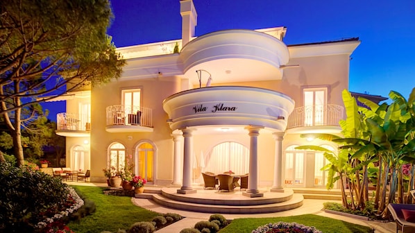 A large, elegant house with a central circular patio, a balcony, and a well-maintained garden.