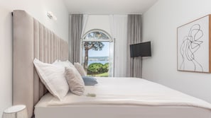 A bedroom with a bed, a TV, and a view of the sea.