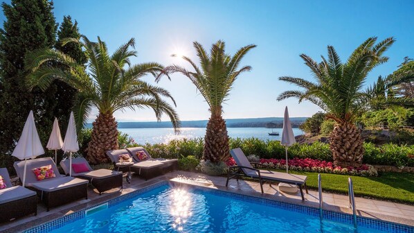 A poolside area with lounge chairs, umbrellas, and a view of the sea.