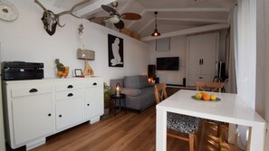 Un soggiorno con un mobile bianco, un divano grigio, un tavolo da pranzo con della frutta e una televisione sullo sfondo.