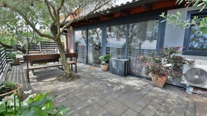 A patio with a bench, potted plants, and a large window overlooking a building.