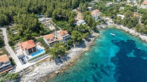 Et kystnære boligområde med huse, en swimmingpool og klart turkis vand.