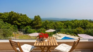 Un balcón con una mesa, dos sillas, una piscina y vistas a árboles y montañas.