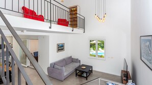 Amplia sala de estar con un sofá gris, una mesa de centro y una escalera que lleva a un balcón.