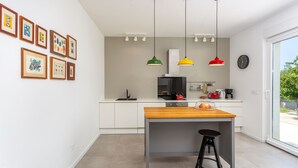 Una cocina moderna con armarios blancos, una isla de madera, lámparas colgantes y cuadros en la pared.
