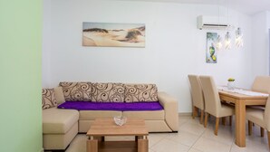 Una sala de estar con sofá, una mesa de centro, una mesa de comedor con sillas, un aire acondicionado y un cuadro en la pared.