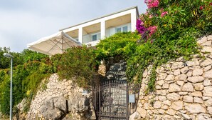 Un edificio moderno con pared de piedra, reja metálica y abundante vegetación.
