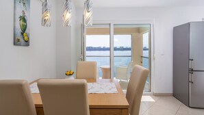 Un comedor con una mesa, sillas, un jarrón de flores y vista al mar a través de un ventanal.