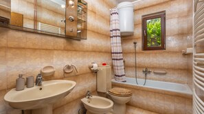 A bathroom with a sink, bidet, toilet, bathtub, and a window with a view of greenery.