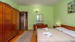 A bedroom with a wooden wardrobe, a bed with rolled towels, a dresser, a mirror, and a painting on the wall.