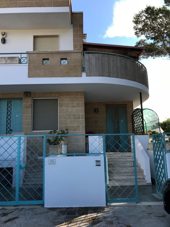 Un edificio residencial de varios pisos con un balcón curvo, una entrada con reja y una escalera que lleva al piso superior.
