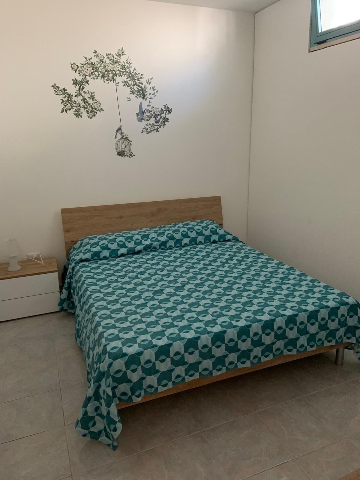 Una camera da letto con un letto in legno, una coperta a motivi, un comodino e un adesivo murale raffigurante un albero con luci appese.