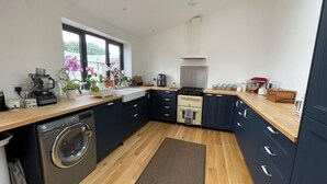 A compact kitchen with a washing machine, a coffee maker, and a stove. - 3 Bedroom Home at Hove with Garden & Cats (Brighton and Hove)