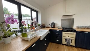 A modern kitchen with a sink, stove, and cabinets. There are potted plants on the counter and a window with a view of greenery outside. - 3 Bedroom Home at Hove with Garden & Cats (Brighton and Hove)