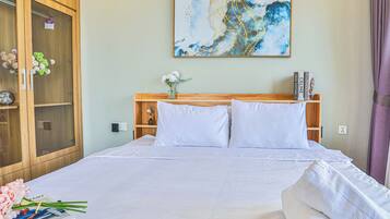 Een net opgemaakt bed met witte lakens, een houten hoofdbord, een vaas met bloemen en een boekenkast vol boeken.