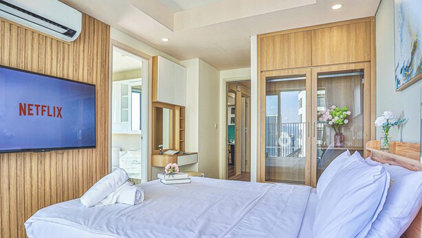 Quarto de hotel com uma cama grande, televisão presa na parede, guarda-roupa de madeira e vista para a cidade pela janela.