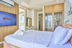 Una camera d'hotel con un letto grande, una TV a parete, un armadio in legno e vista sulla città dalla finestra.