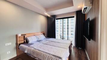 A modern hotel room with a large bed, a flat-screen TV, and a view of a cityscape through the window.